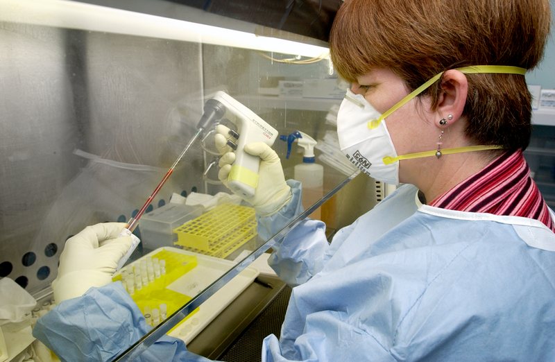 Laboratory worker in a gown, respirator and gloves at a biosafety cabinet